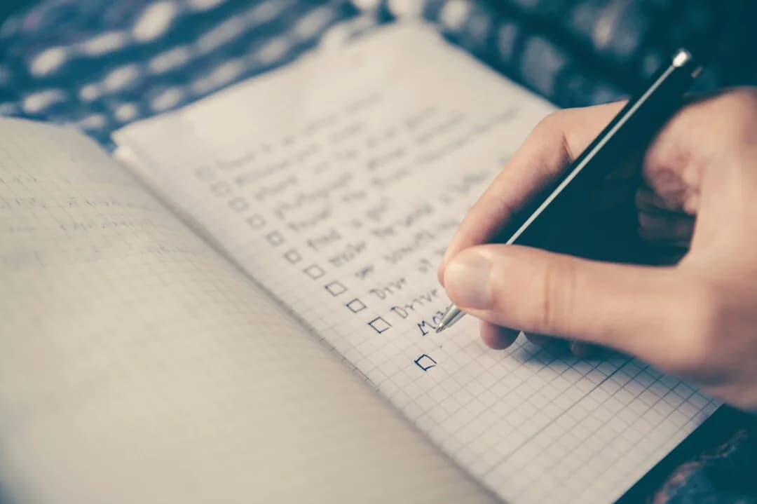 A hand writing a checklist in a notebook.
