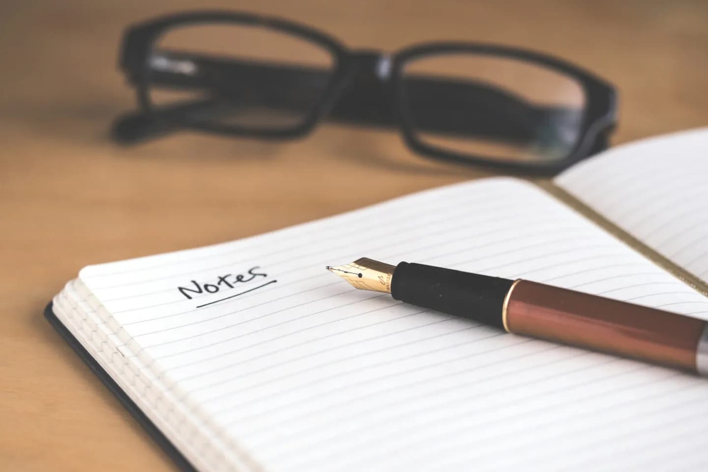 A fountain pen on a notebook with glasses behind it.