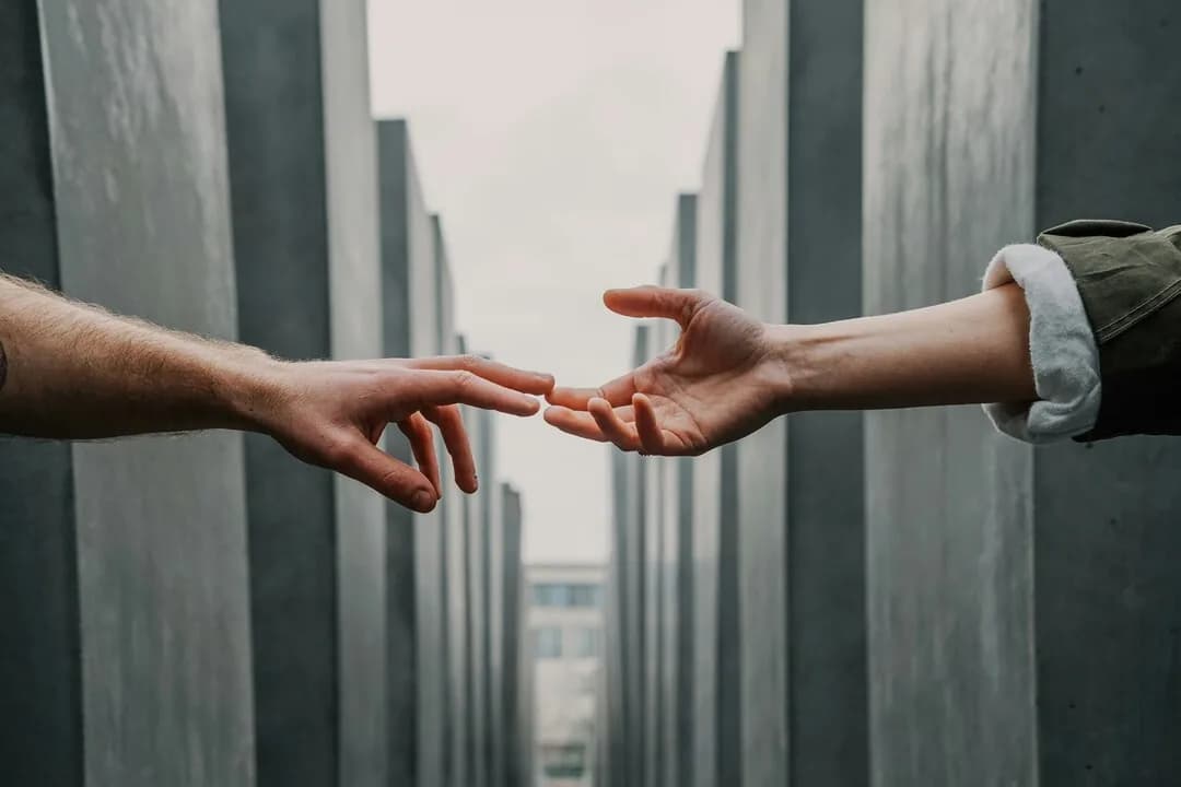 Two hands reaching towards each other between buildings.