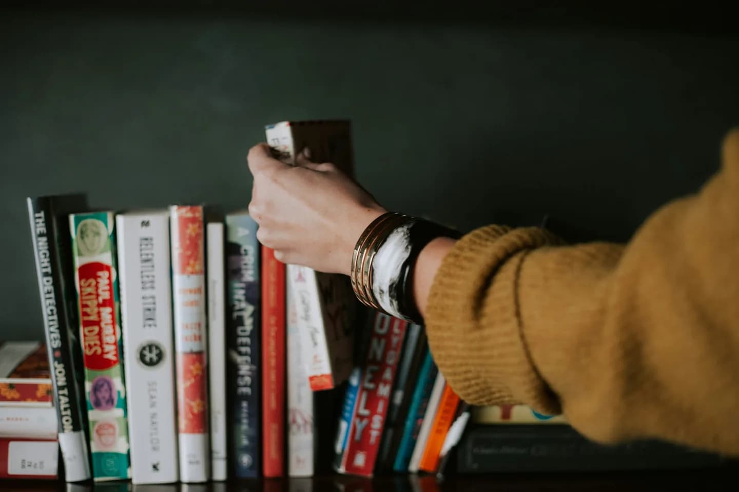 A hand selecting a book from a shelf.