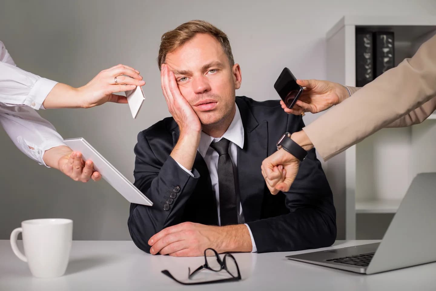 A person at a desk surrounded by hands offering requests.