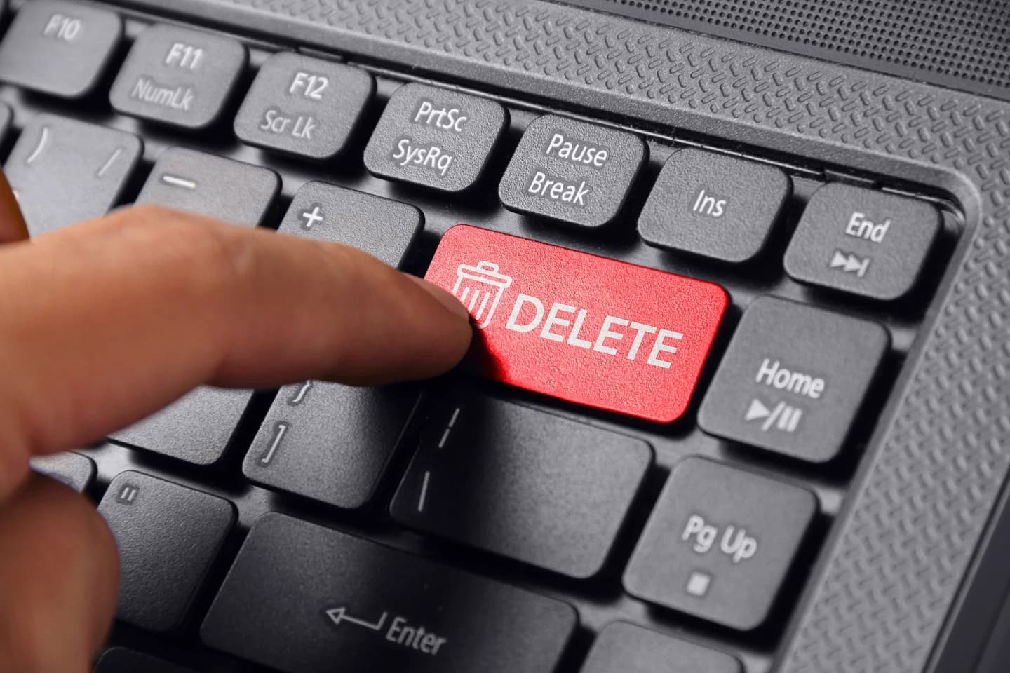 A finger pressing a red Delete key on a keyboard.
