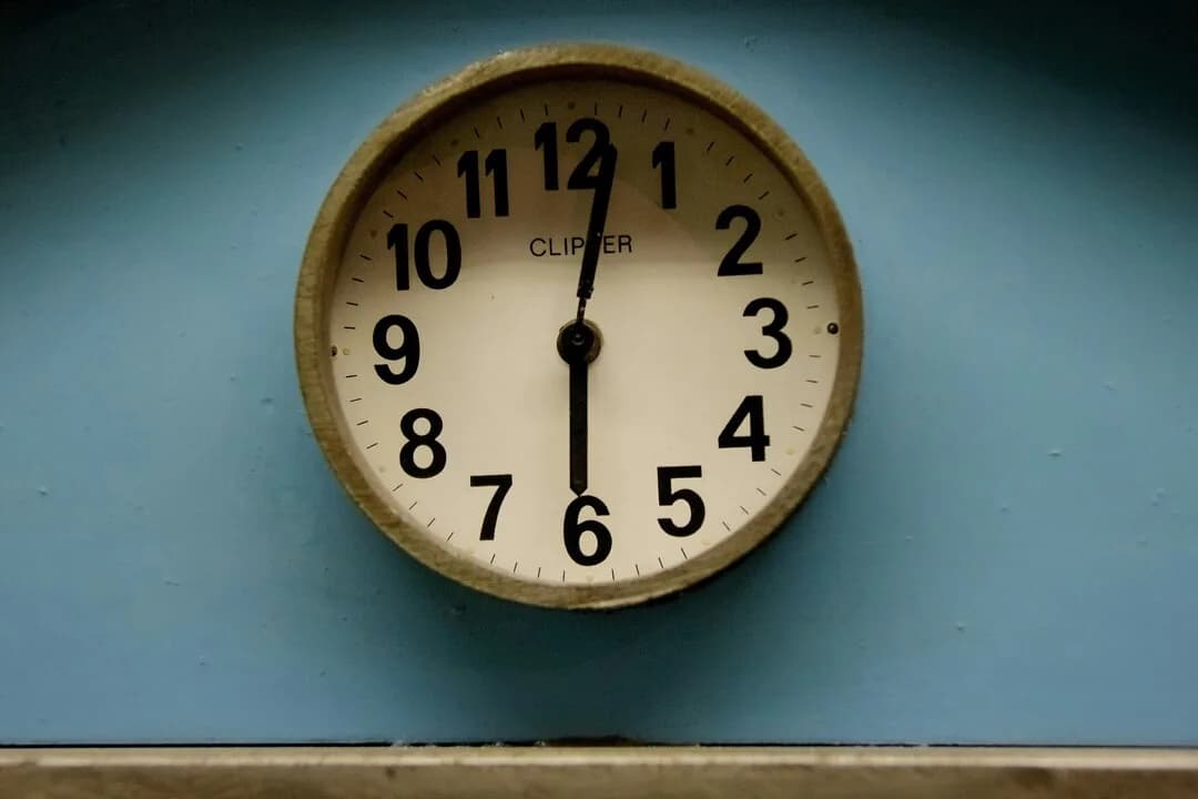 An analogue wall clock against a blue wall.