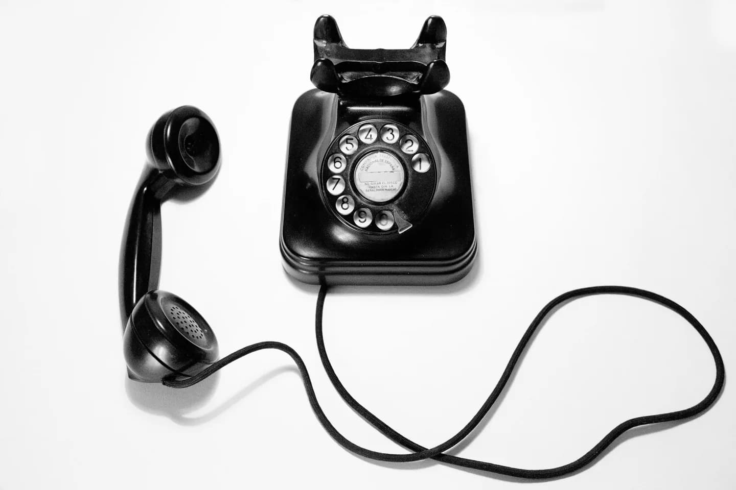 A black rotary telephone with its receiver off the hook.