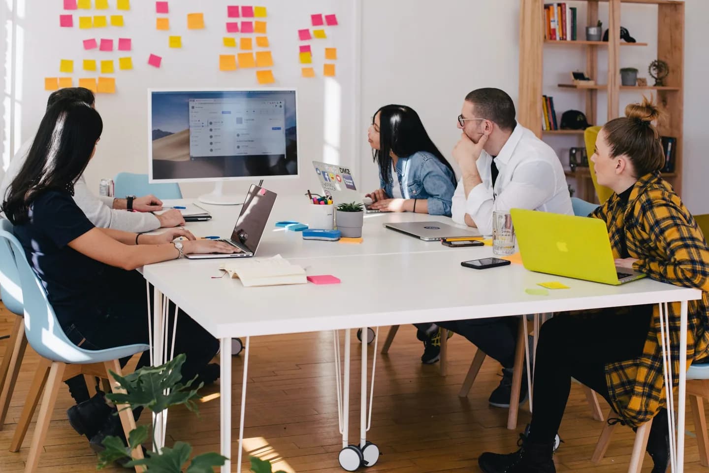 A team working around a table beneath a wall of sticky notes.