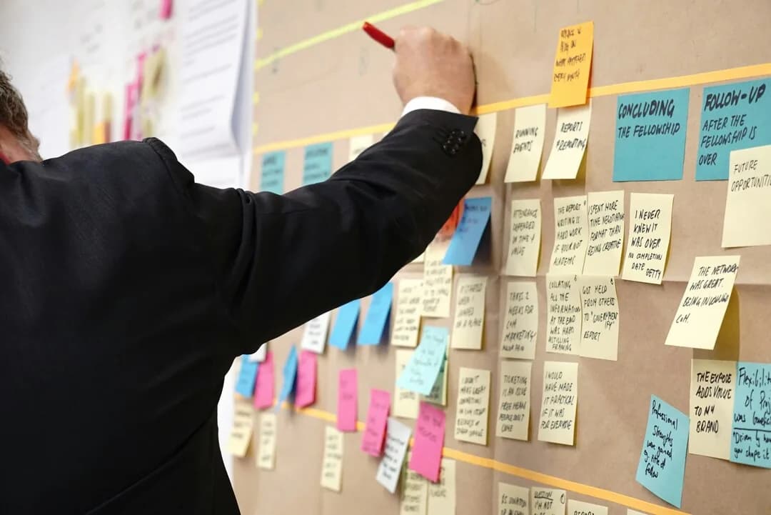 A person arranging sticky notes on a wall-mounted board.